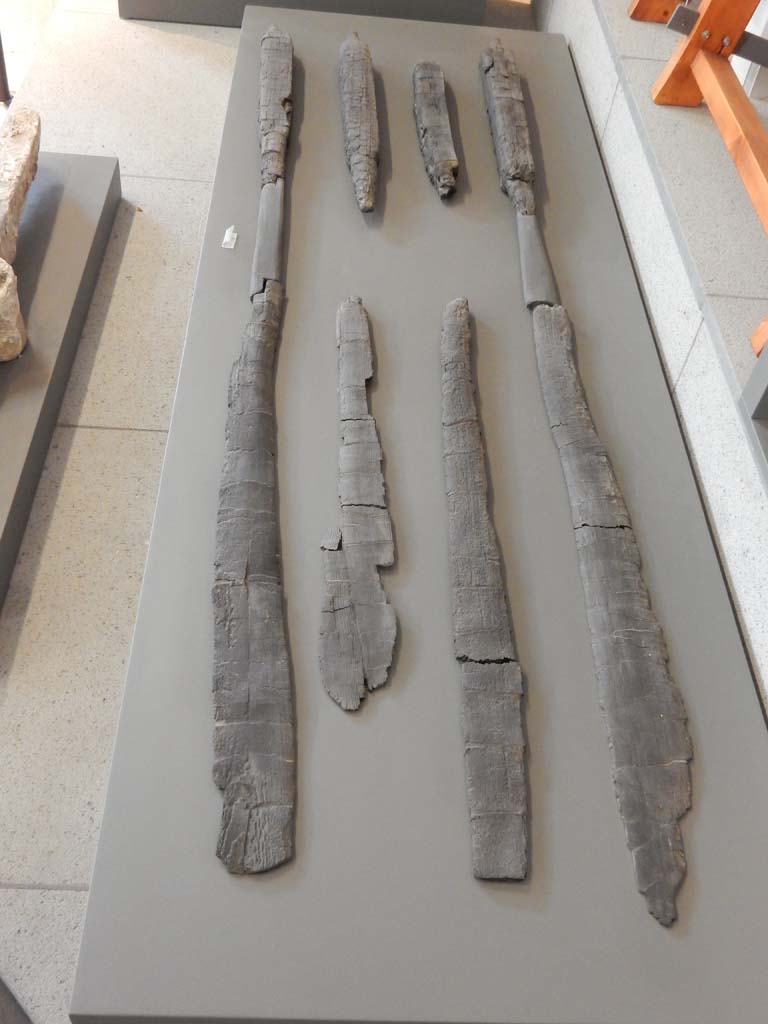 Herculaneum, June 2019. Carbonised wooden oars.
Six oars were found in the bath building in Insula Occidentalis at Herculaneum, along with parts of other boats, a red prow in the shape of a serpent, a wooden rudder and a pile of planking ready for use. This shows that the bath building was not in use at the time of the eruption but had been transformed into a space for laying-up boats and storing maritime equipment. Photo courtesy of Buzz Ferebee.
